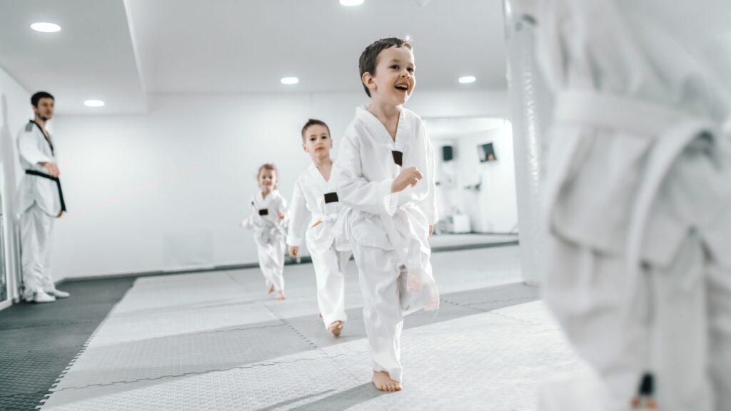 Des jeunes enfants s'exercent aux arts martiaux en courant sur un tatami devant leur entraineur.
